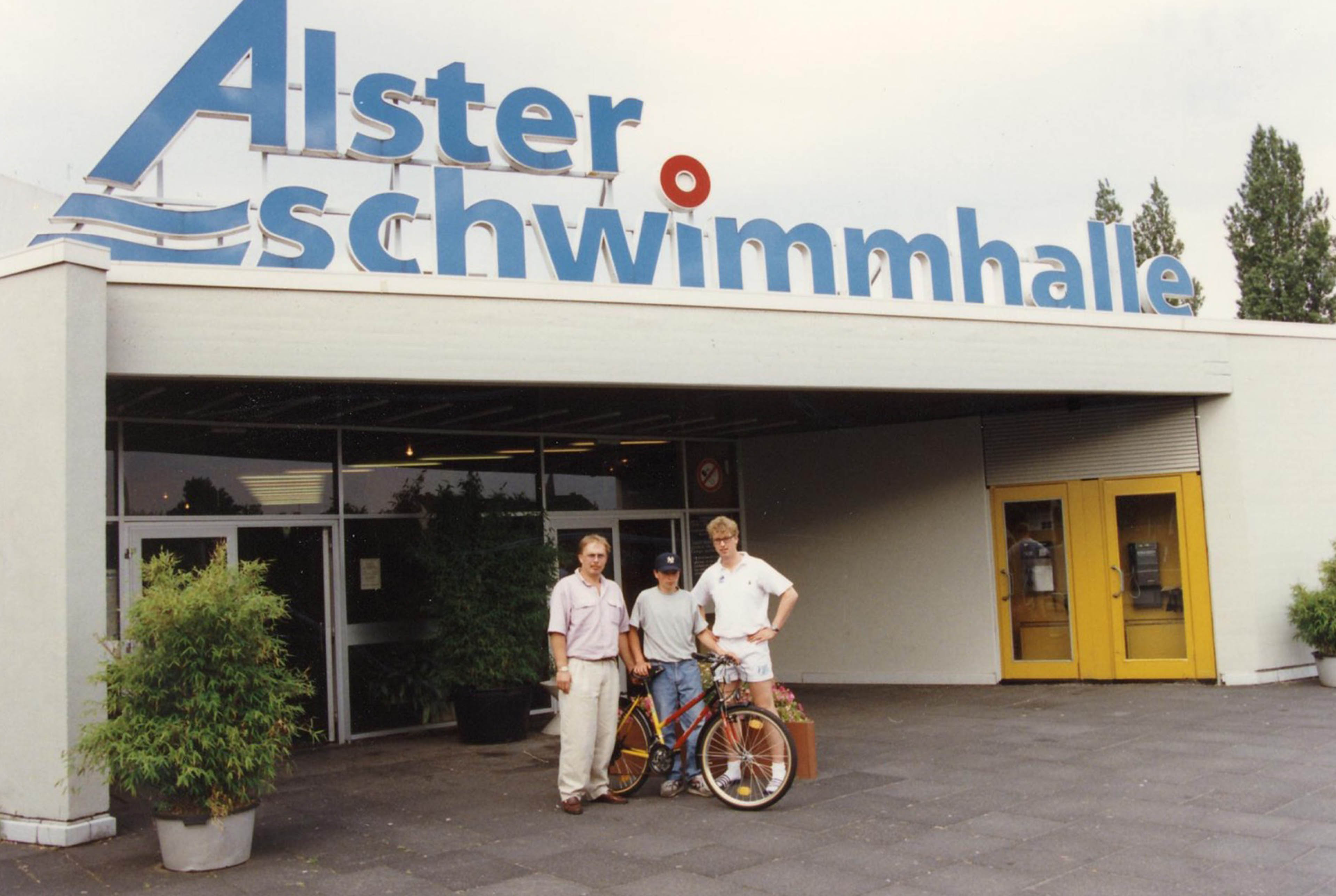 Drei Personen stehen mit einem Fahrrad vor dem ehemaligen Eingang der Alster-Schwimmhalle