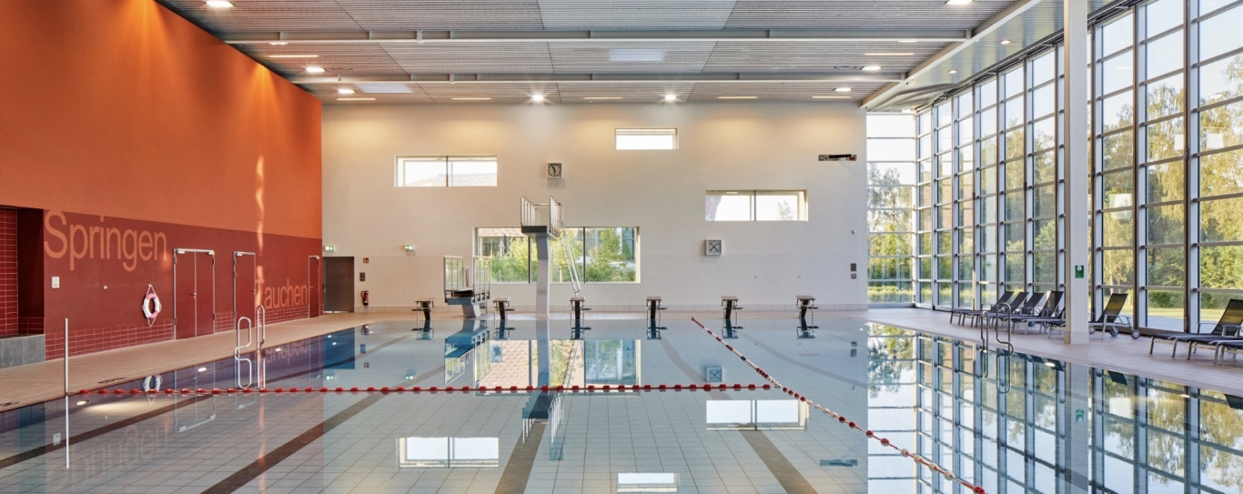 Schwimmbad mit Bahnen, Startblöcken und Fensterfront rechts