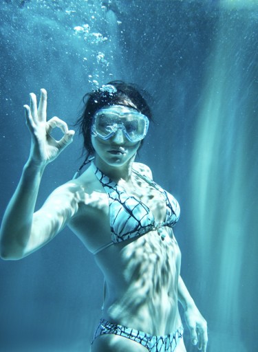 Frau im Bikini mit Taucherbrille zeigt unter Wasser das Zeichen für "ok"