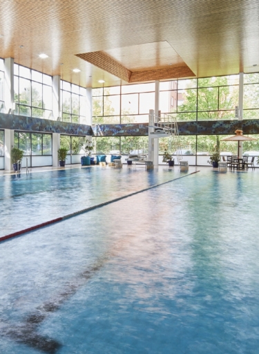 Schwimmbad mit Bahnen, Startblöcken, Sprungbrett und Fensterfront