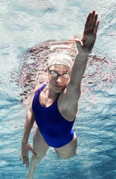 Frau im blauen Badeanzug krault Unterwasser