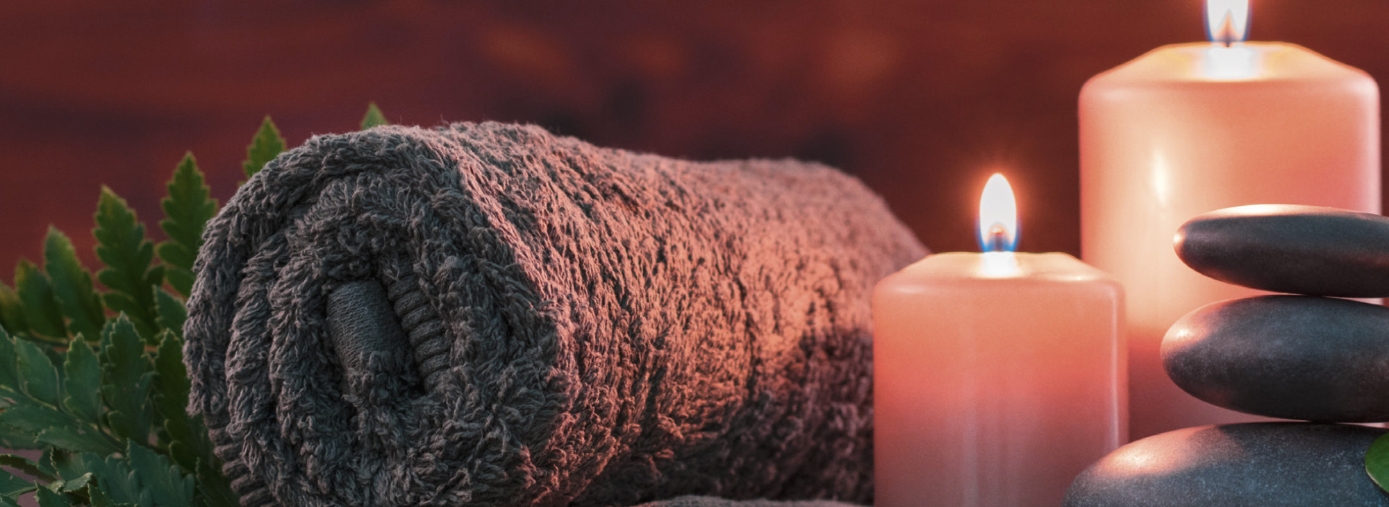 Eingerolltes Handtuch, brennende Kerzen und aufeinander liegende Steine