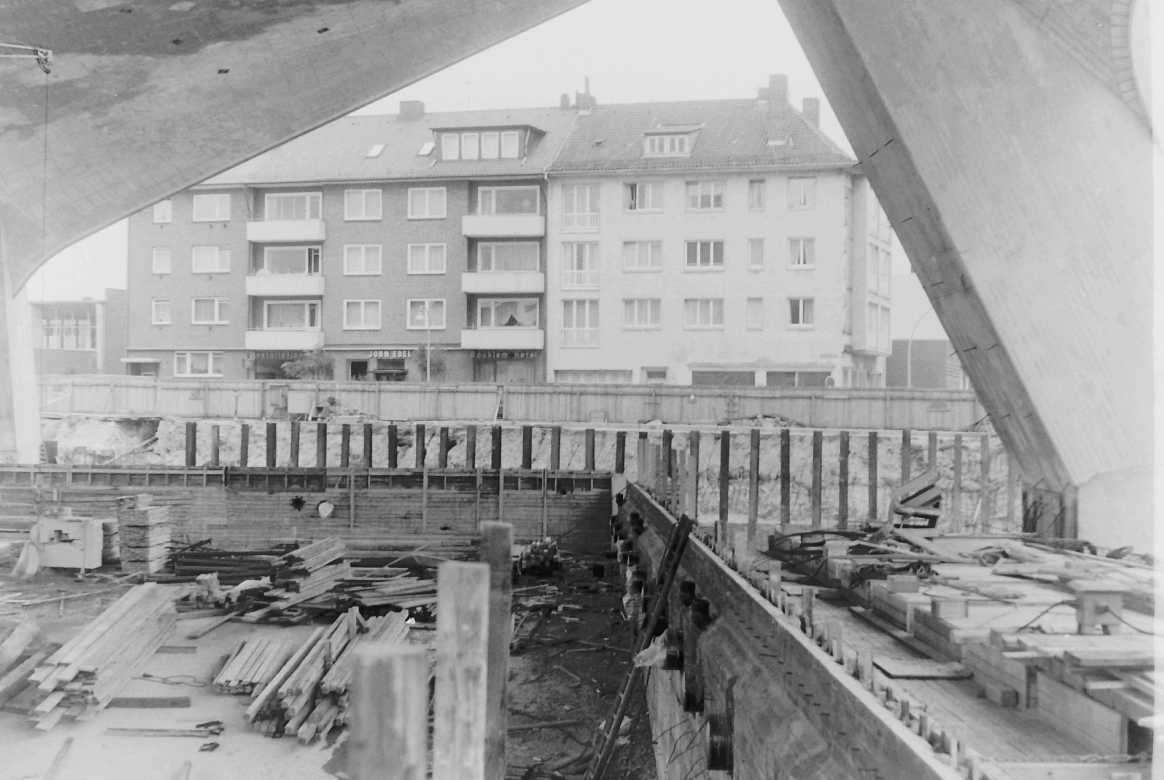 Blick auf Baustelle mit Haufen von Holzbrettern, im Hintergrund eine Wohnblock