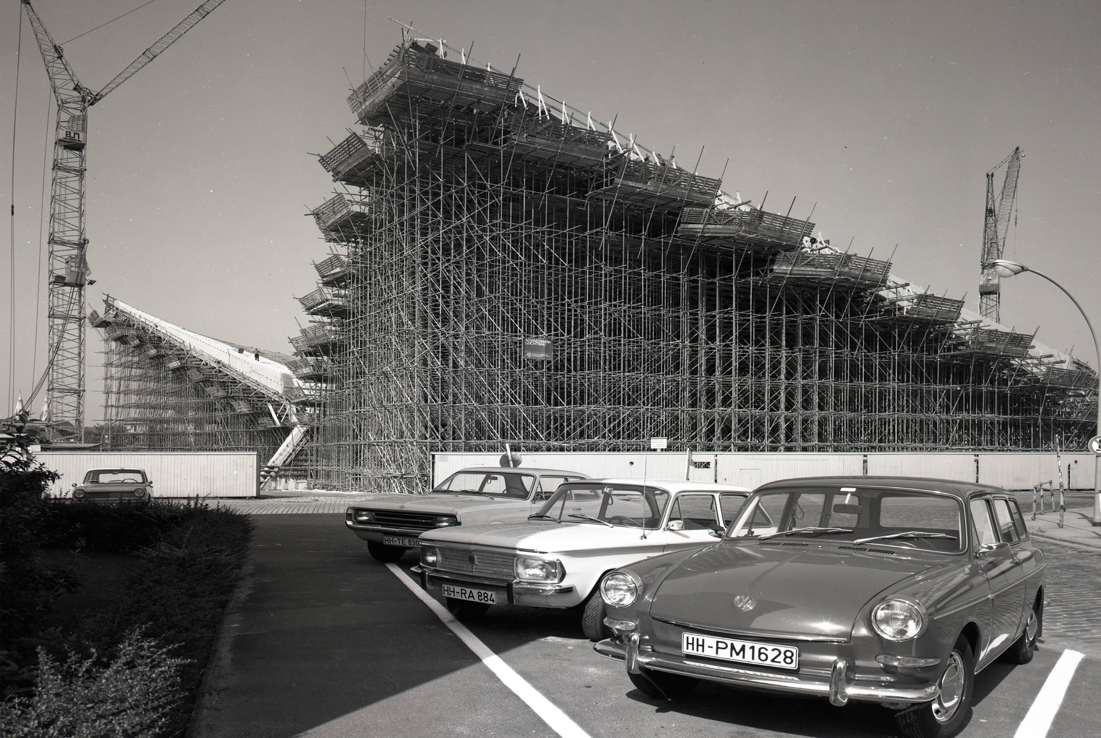 Blick vom Parkplatz auf drei Autos und im Hintergrund die Baukonstruktion der Alster-Schwimmhalle