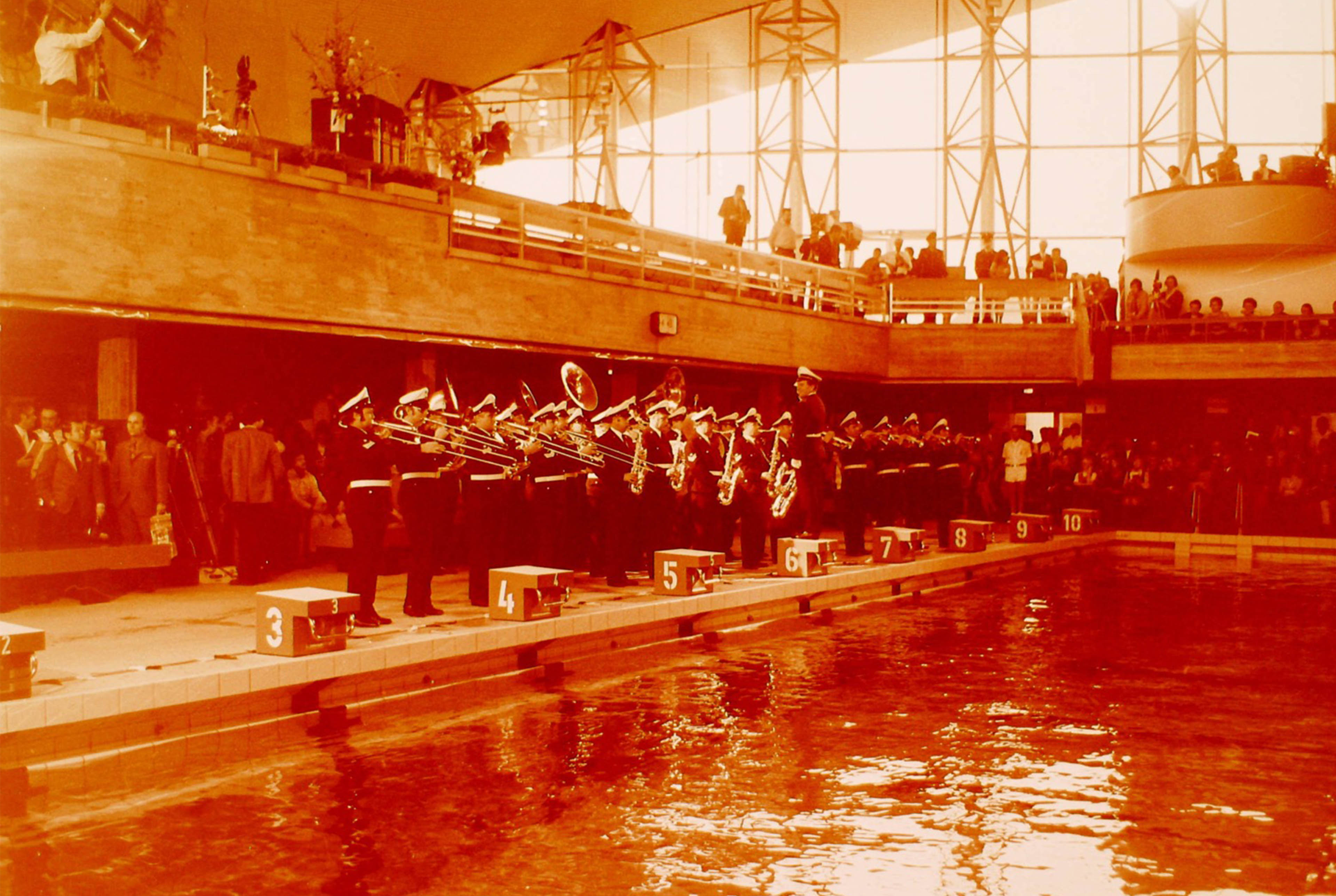 Viele Menschen mit Blasinstrumenten machen vor einem Schwimmbecken Musik