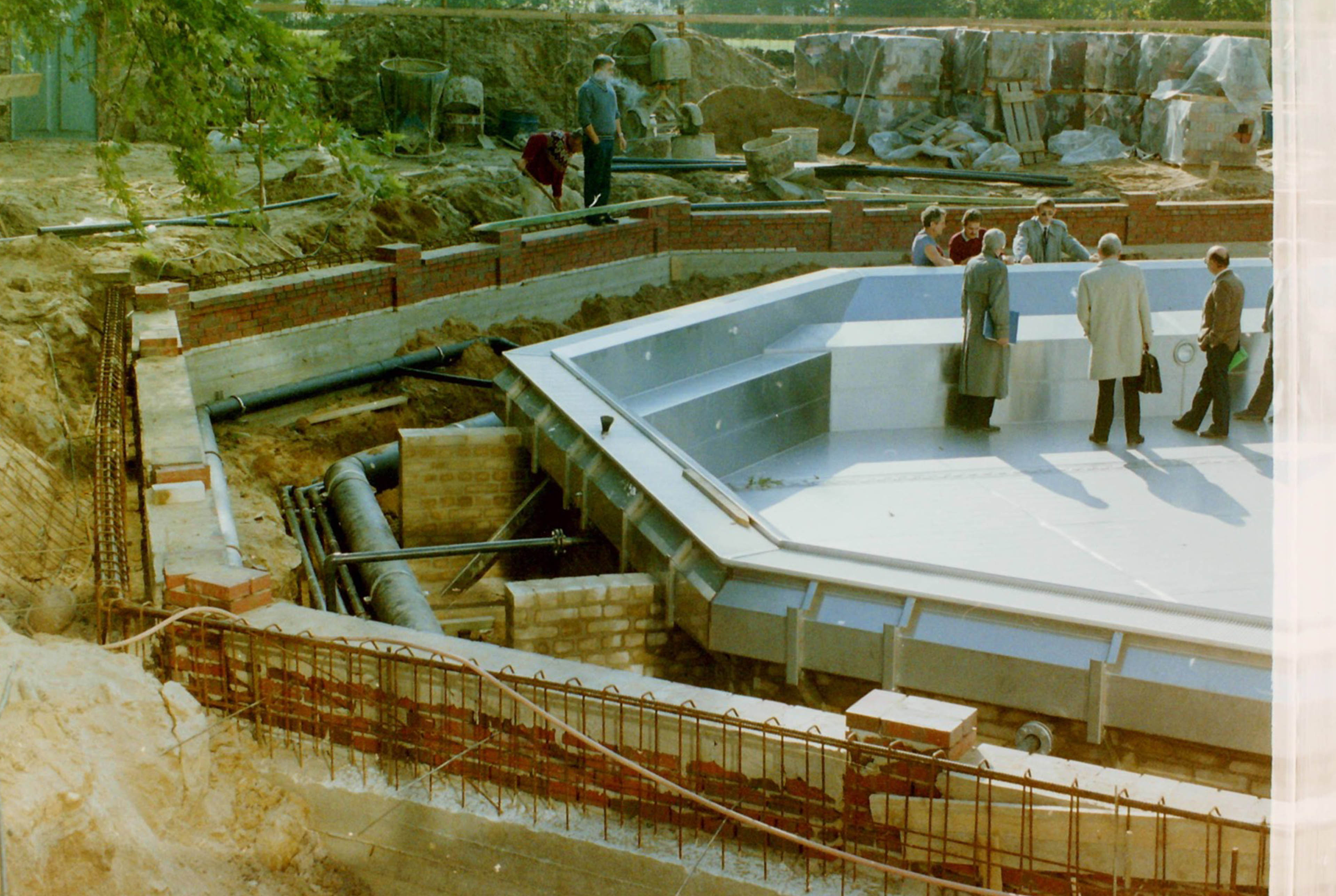 Ein paar Männer stehen in Anzügen in einem leeren Becken auf einer Baustelle