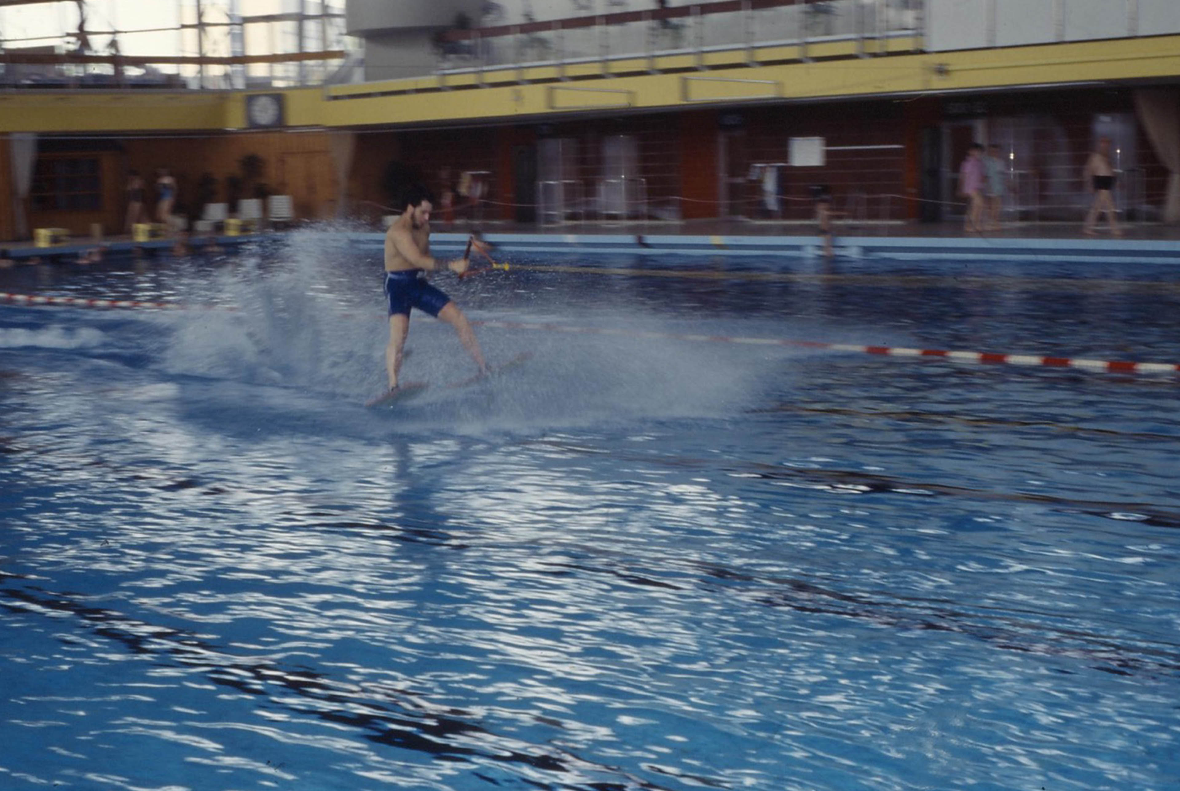 Mann auf Wasserski fährt übers Wasser im Schwimmbecken