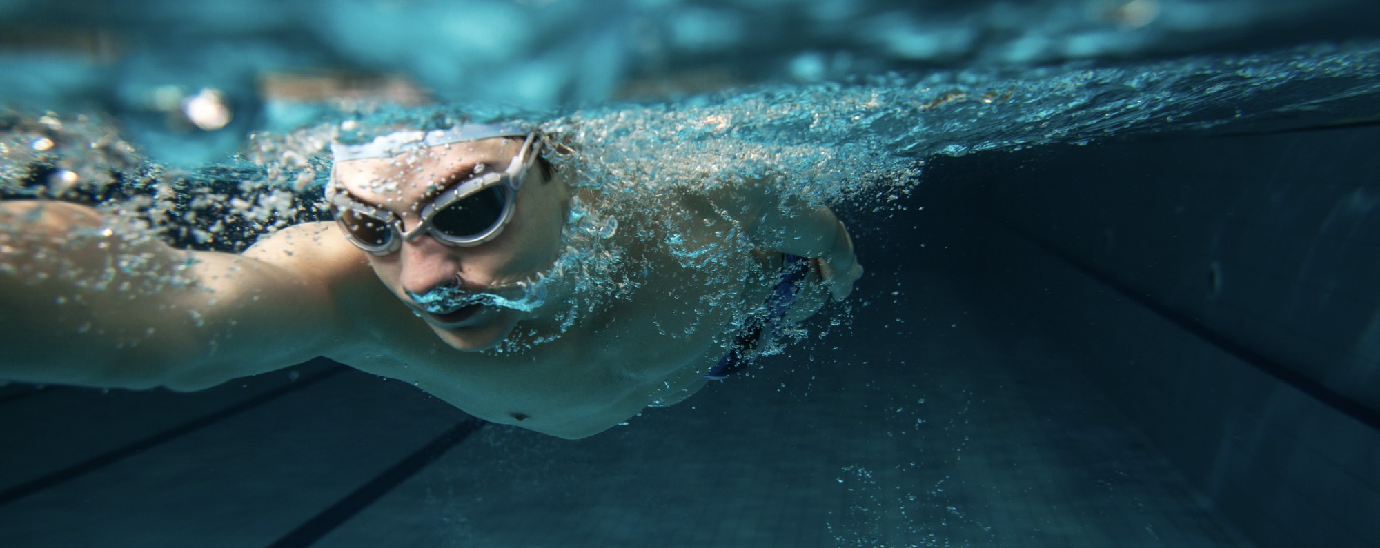 Mann mit weißer Badekappe und Schwimmbrille unter Wasser