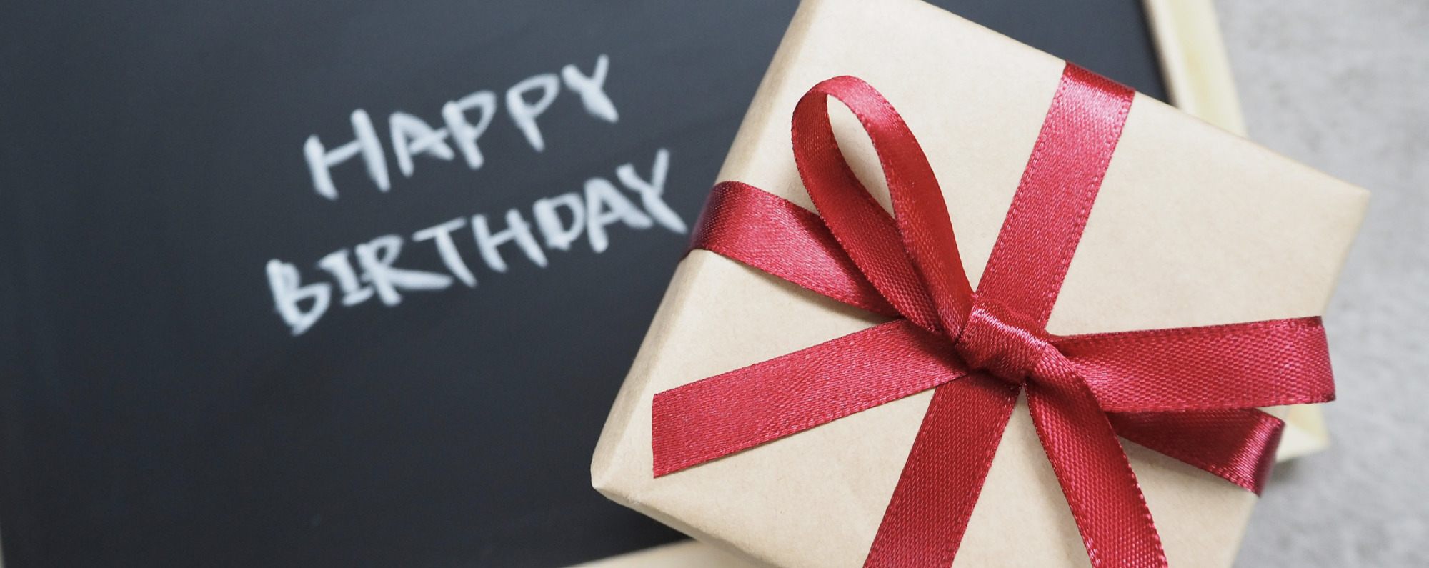 Happy Birthday mit Kreide auf Tafel geschrieben und ein Geschenk davor