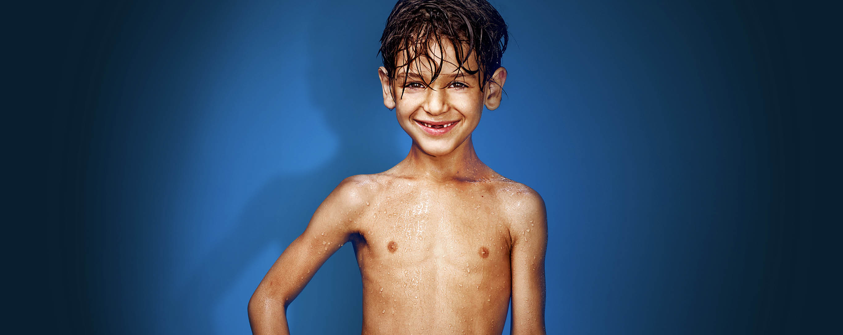 Junge mit gelber Badehose vor blauem Hintergrund