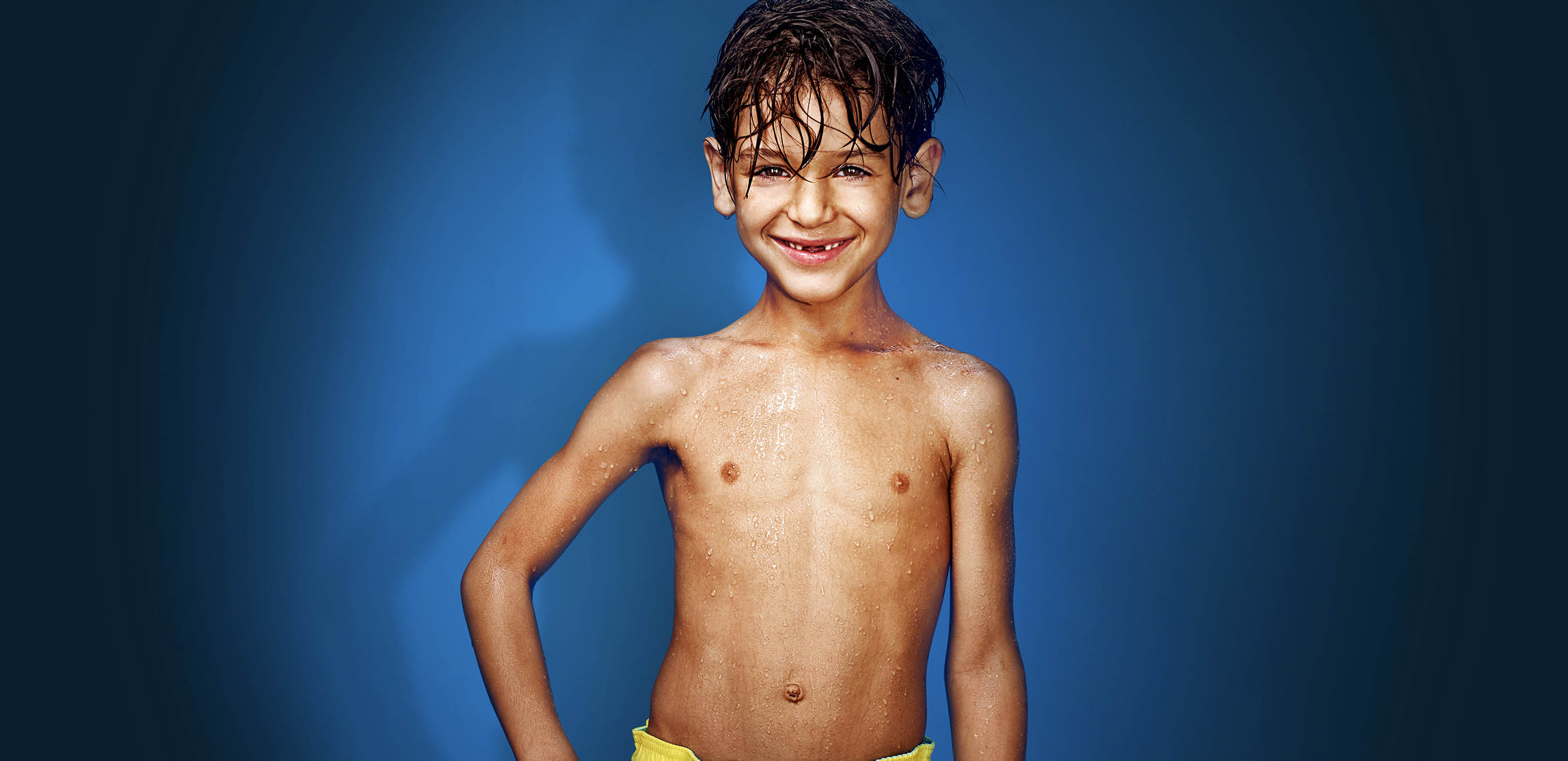 Junge mit gelber Badehose vor blauem Hintergrund