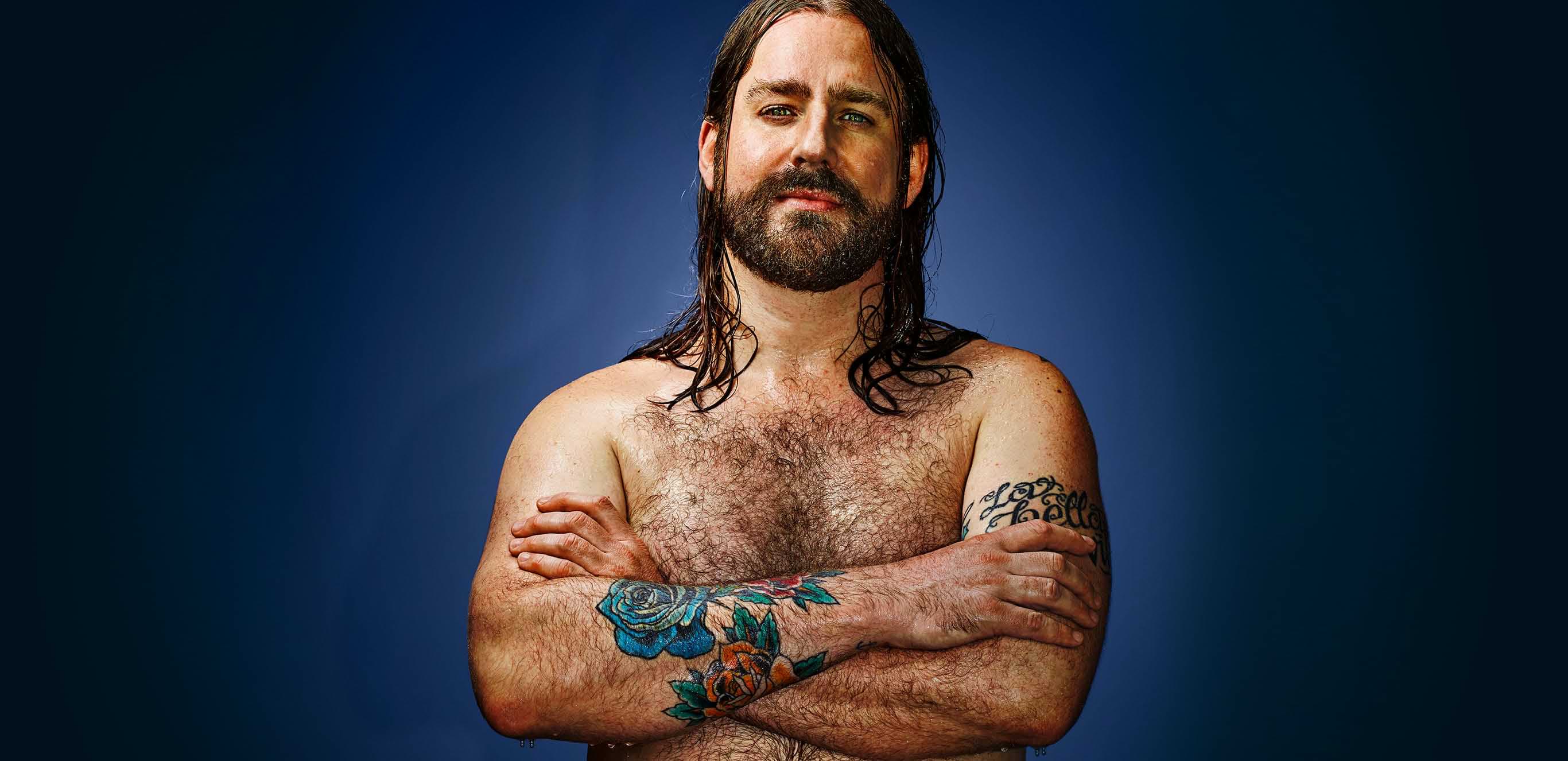 Mann mit Tattoos auf den verschränkten Armen in Badehose.