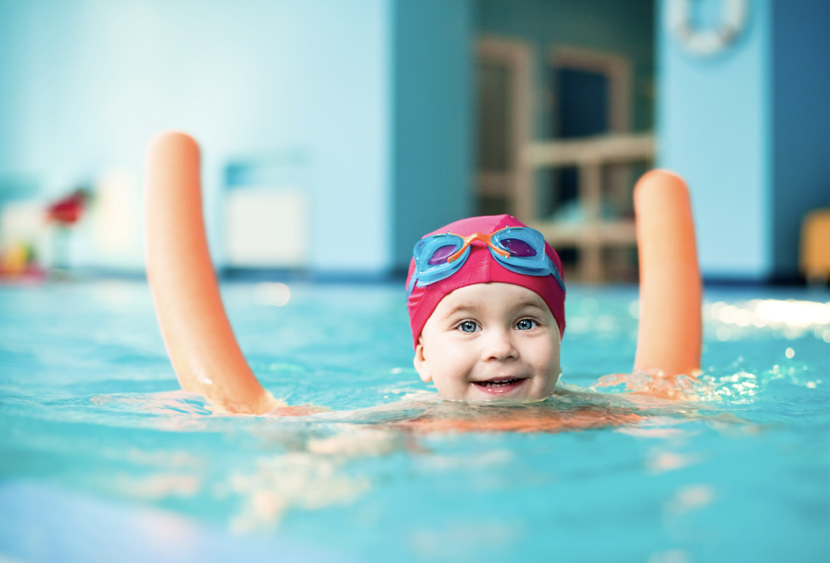 Kleinkind mit Badekappe und Brille auf Schwimmnudel im Wasser