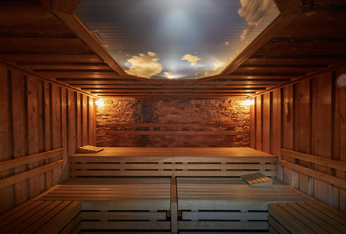 Holzsauna mit Steinwand und blauem Himmel