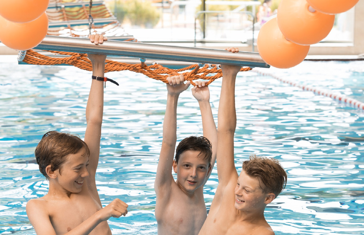 Kinder im Wasser halten sich mit den Händen an Spielgerät fest