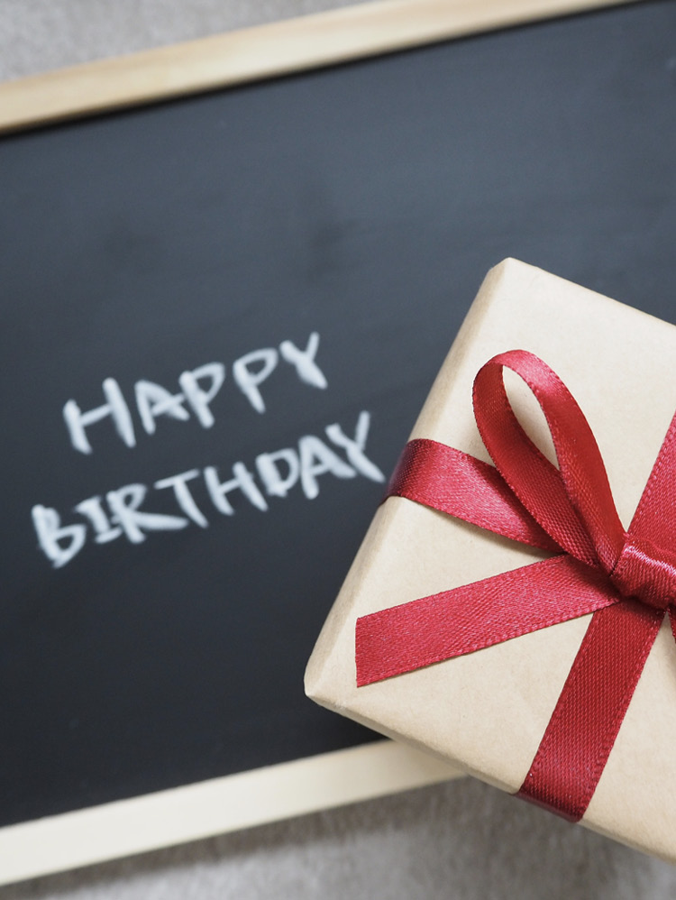 Happy Birthday mit Kreide auf Tafel geschrieben und ein Geschenk davor