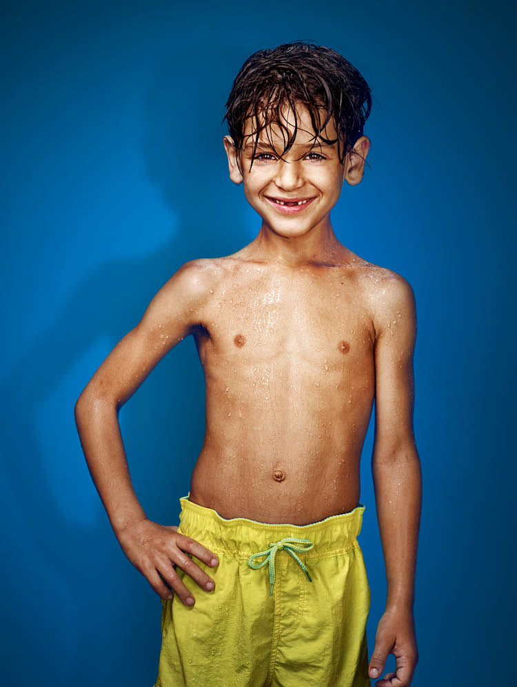 Junge mit gelber Badehose vor blauem Hintergrund