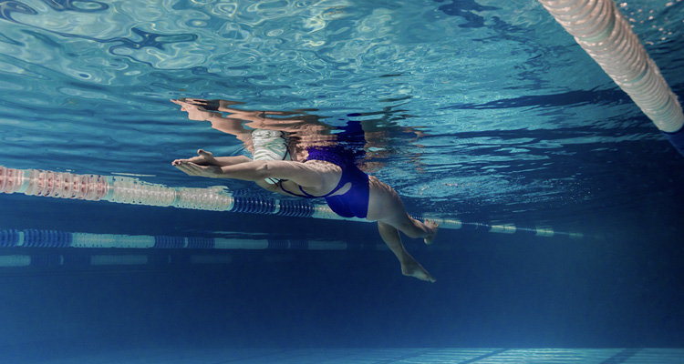 Frau mit blauem Badeanzug gleitet unter Wasser