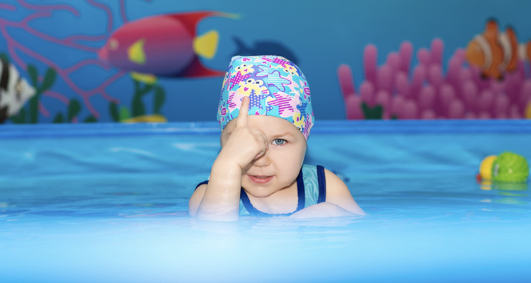 Kleinkind mit bunter Badekappe im Wasser