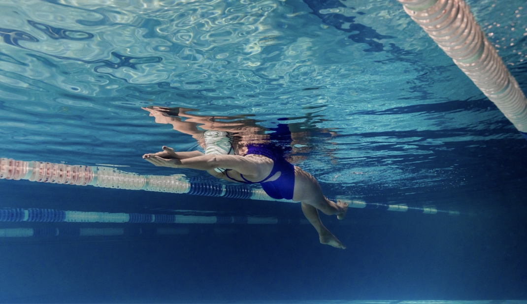 Frau mit blauem Badeanzug gleitet unter Wasser