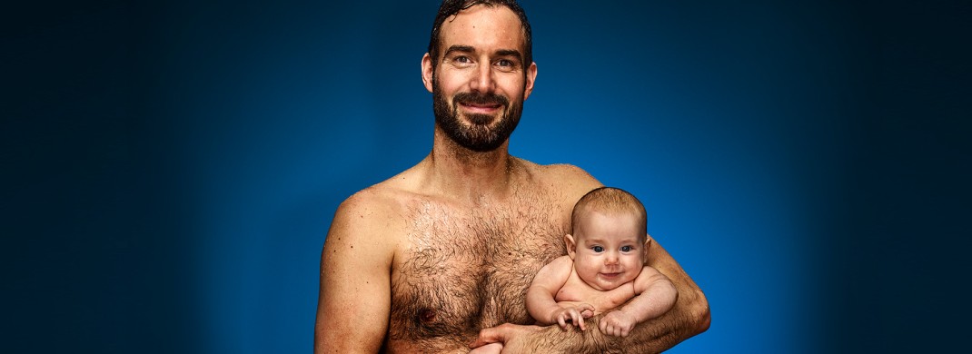 Mann in Schwimmkleidung mit Baby im Arm