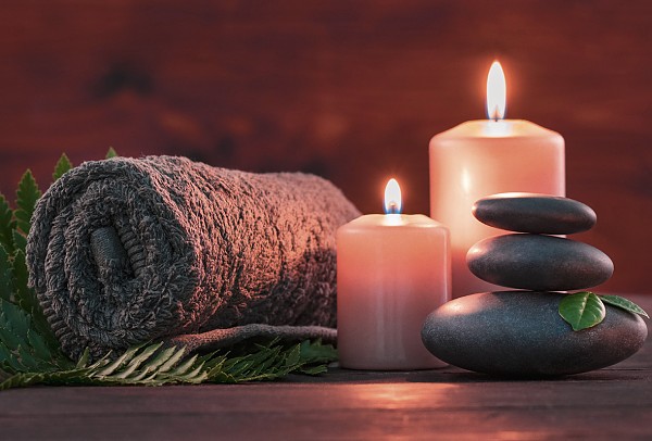 Eingerolltes Handtuch, brennende Kerzen und aufeinander liegende Steine