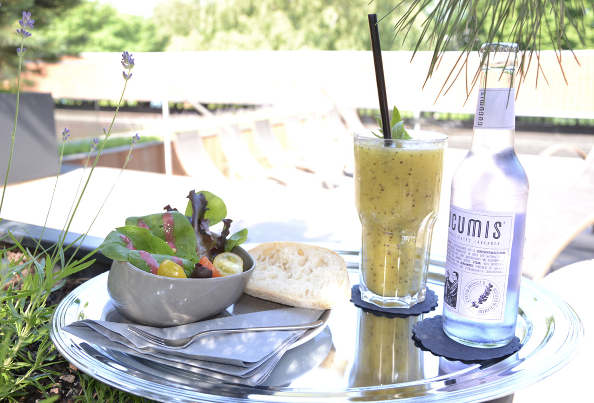 Tablett mit Salat, Saft und Wasser draußen in der Sonne.