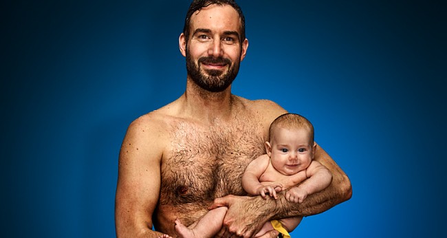 Mann in Schwimmkleidung mit Baby im Arm