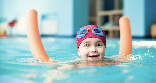 Kleinkind mit Badekappe und Brille auf Schwimmnudel im Wasser