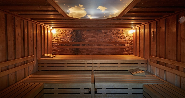 Holzsauna mit Steinwand und blauem Himmel