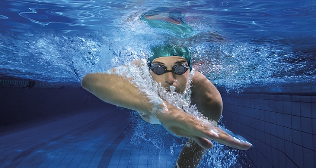 Mann mit grüner Badekappe und Schwimmbrille unter Wasser