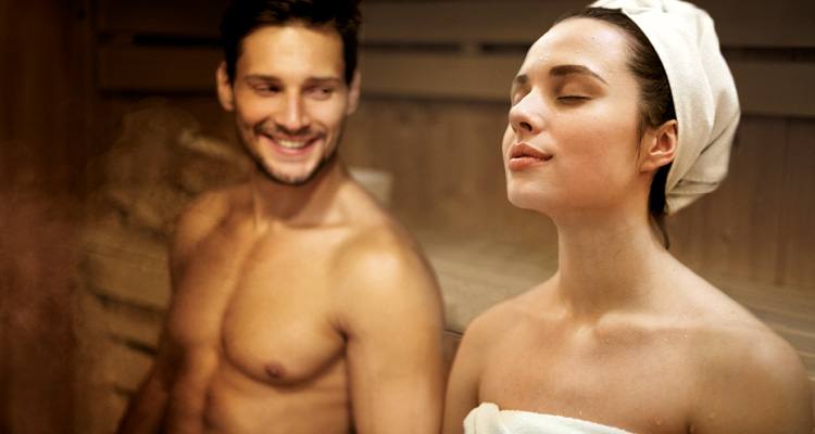 Lächelnder Mann und Frau mit Kopfhandtuch in der Sauna.