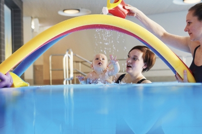 Zwei Frauen mit einem Baby im Wasser unter Bogen aus Schwimmnudeln