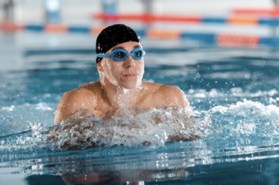 Mann mit schwarzer Badekappe und Schwimmbrille beim Luftholen an der Wasseroberfläche