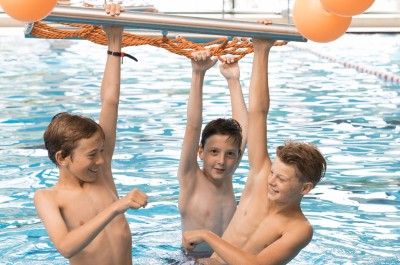Drei Jungs hängen fröhlich an einem Klettergerüst im und über dem Wasser.