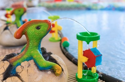 Nahaufnahme des Beckenrands aus dem Kinderbereich. Wasserspuckende Dinosaurier setzen festinstaliertes Kinderspielzeug durch Wasser in Bewegung.