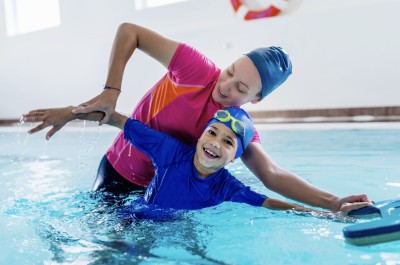 Schwimmlehrerin zeigt Kind die richtige Bewegung beim Kraueln