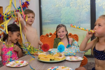 Fünf kleine Kinder feiern fröhlich mit Luftschlangen und Kuchen, an einem Tisch sitzend, Kindergeburtstag