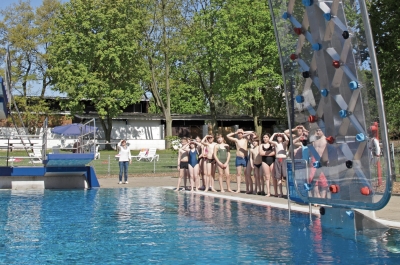 Freibadbecken mit Kletterwand und Kindern am Beckenrand.