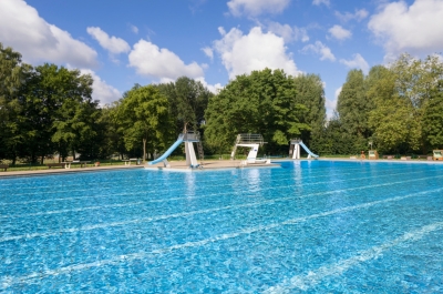 Freibadbecken an einem Sommertag mit Bäumen im Hintergrund.