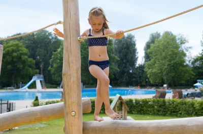 Kleines Mädchen klettert auf Baumstämmen.