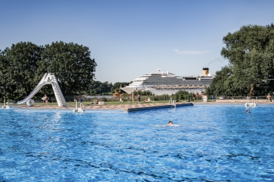 Freibadbecken mit Rutsche und ein Schiff ist in der Ferne zu erkennen.