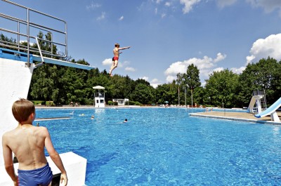 Becken mit Sprungturm und Rutsche und Kindern im Sommer.