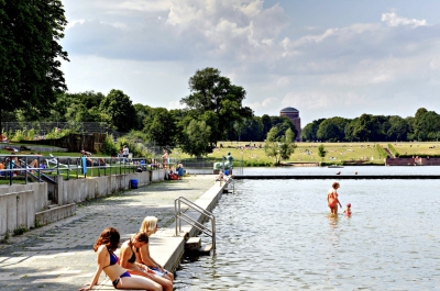 Freibadbecken mit Beckenrand und Menschen tauchen ihre Füße ins Wasser.