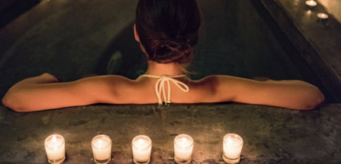 Frau am Beckenrand der Therme, auf dem Kerzen stehen